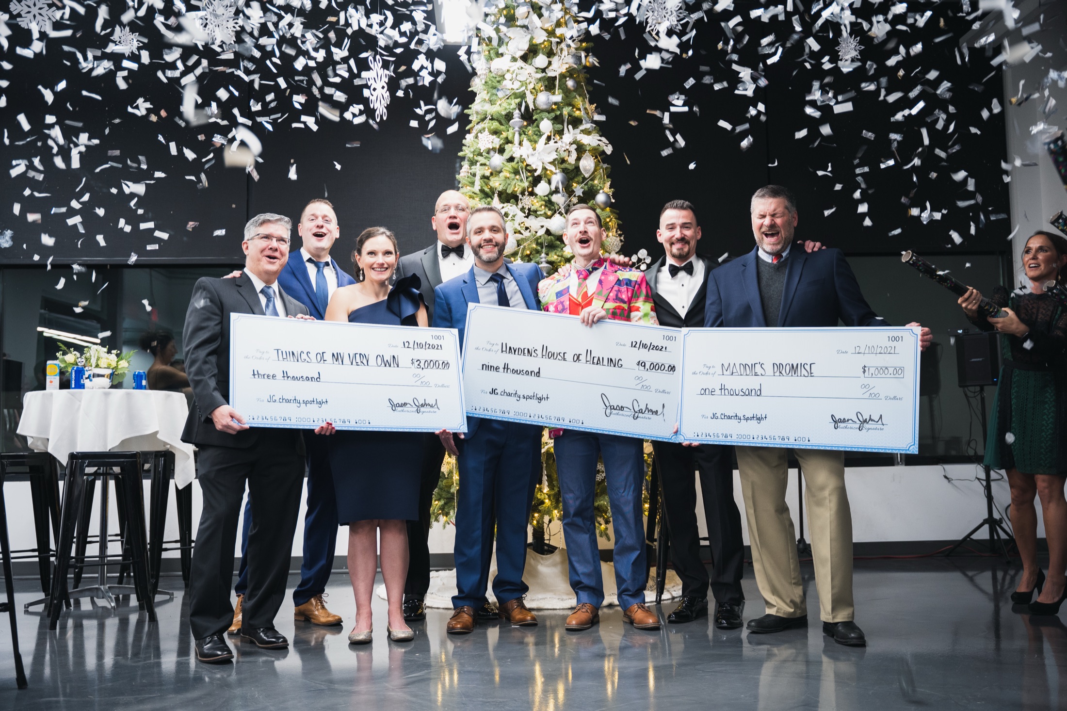 Jahnel Group team holding three oversized charity checks under confetti at the holiday party